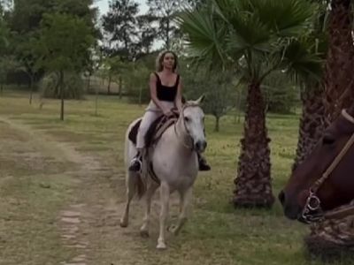 Christina Invernizzi is riding a white horse in the field.